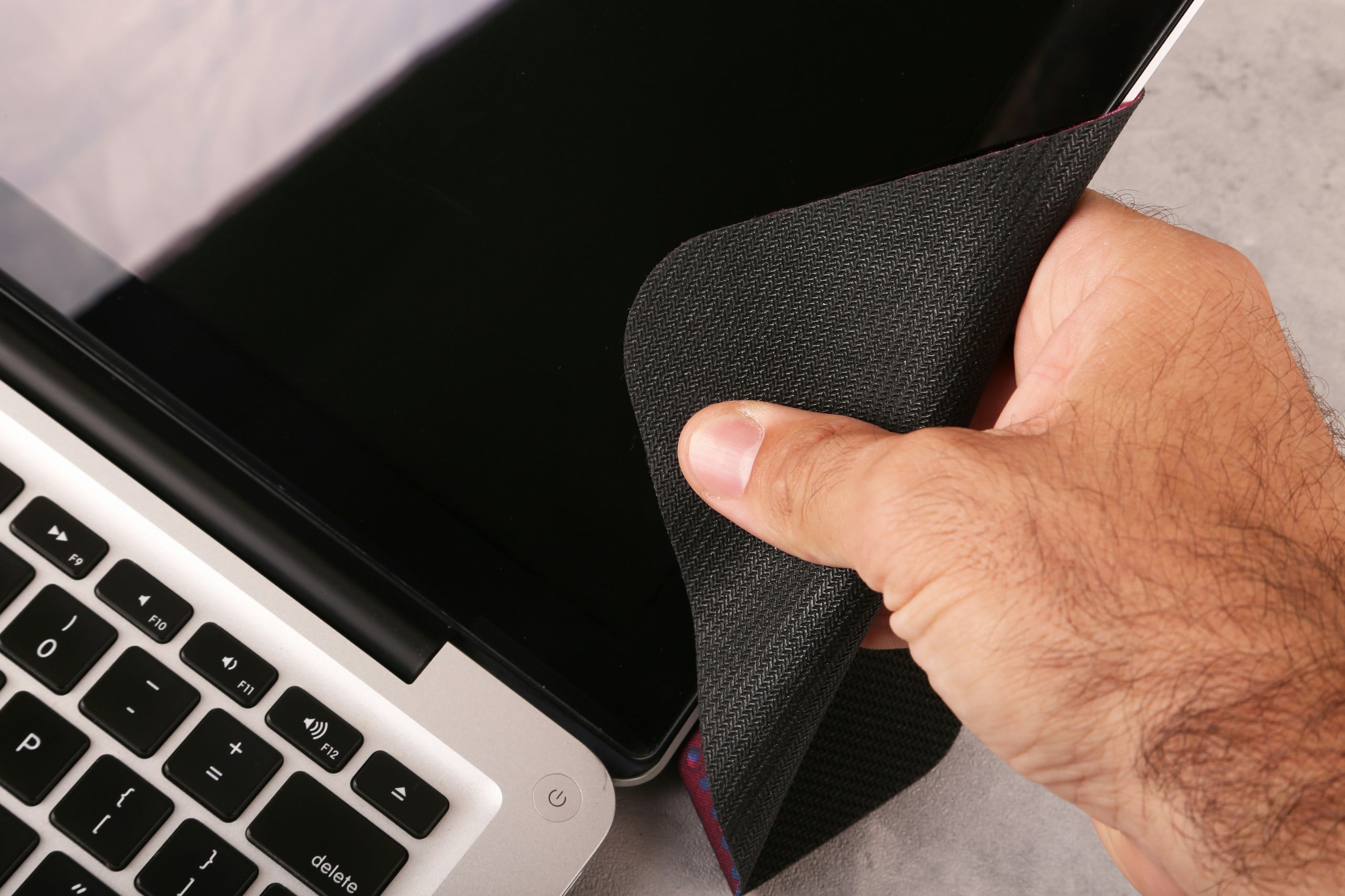 hand holding a cloth to clean a laptop computer