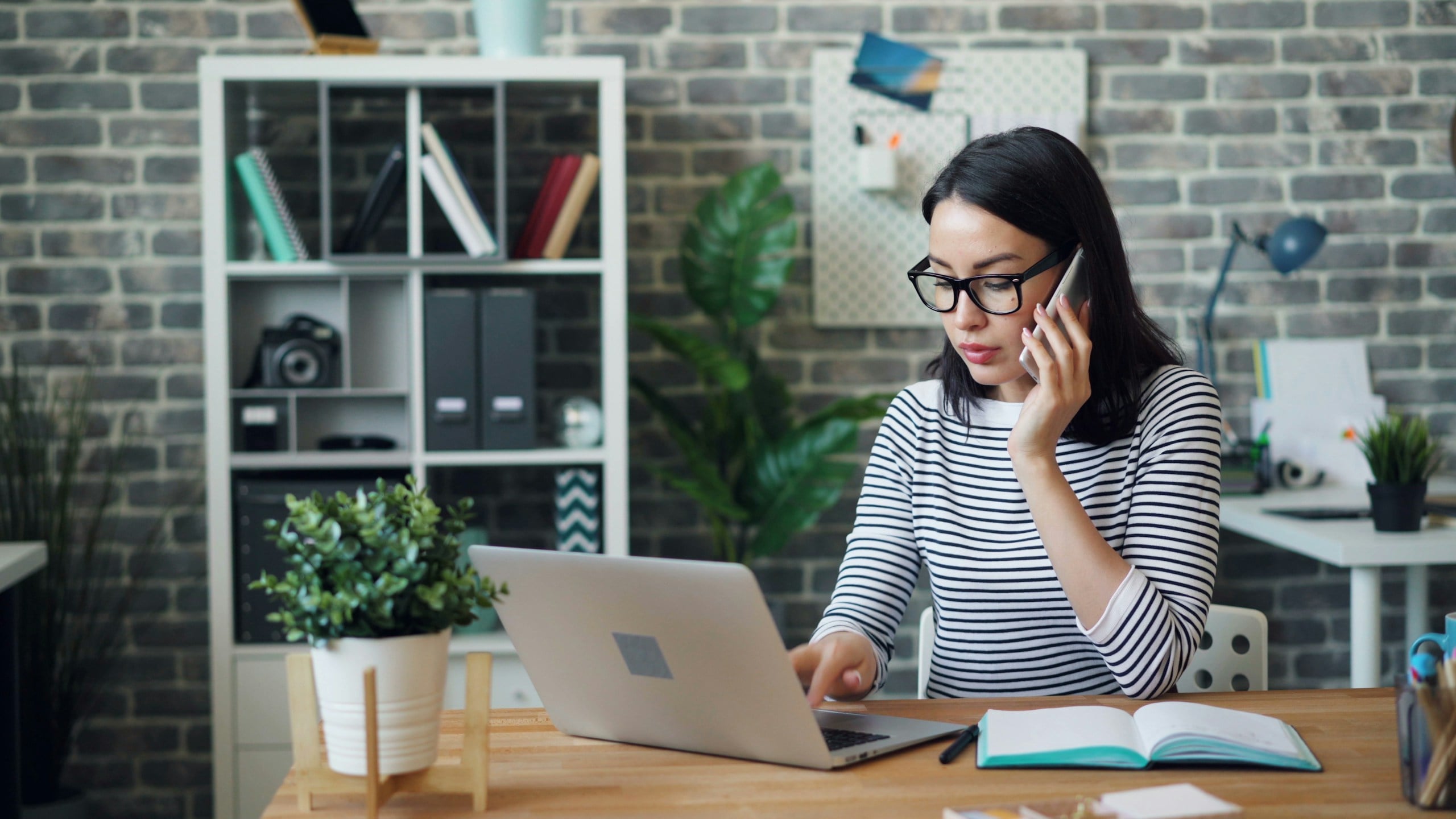 Female office worker talking on mobile phone and using laptop then taking notes