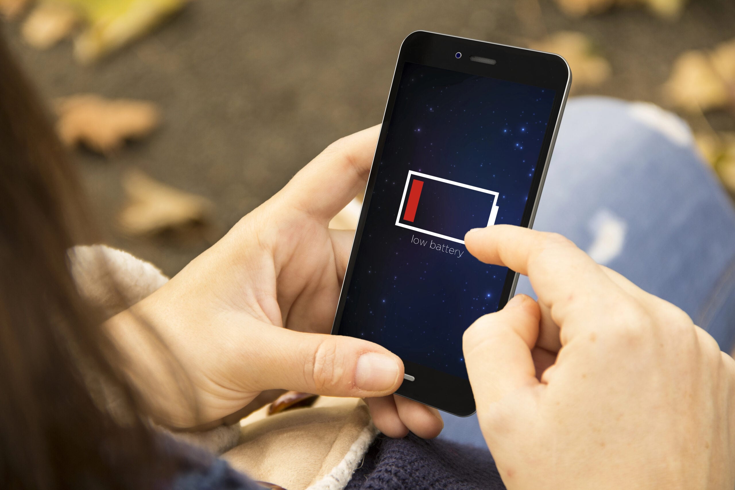 A hand holding a smartphone showing low battery.