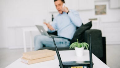 selective focus of black plugged router on white table and businessman talking on smartphone