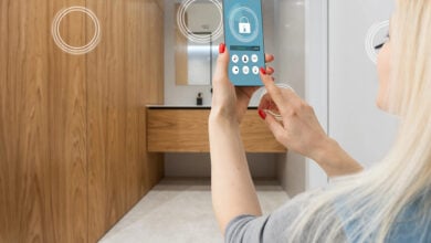 Smart home automation app on smartphone hold by female hand with home interior in background.