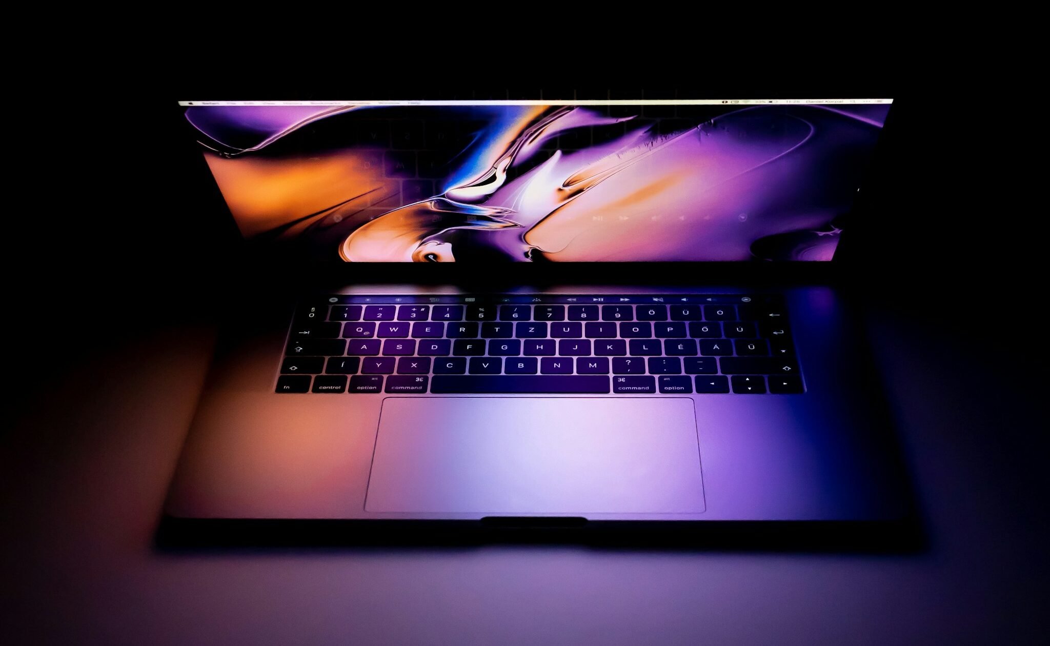 A laptop sitting open in the dark with a colorful screensaver.