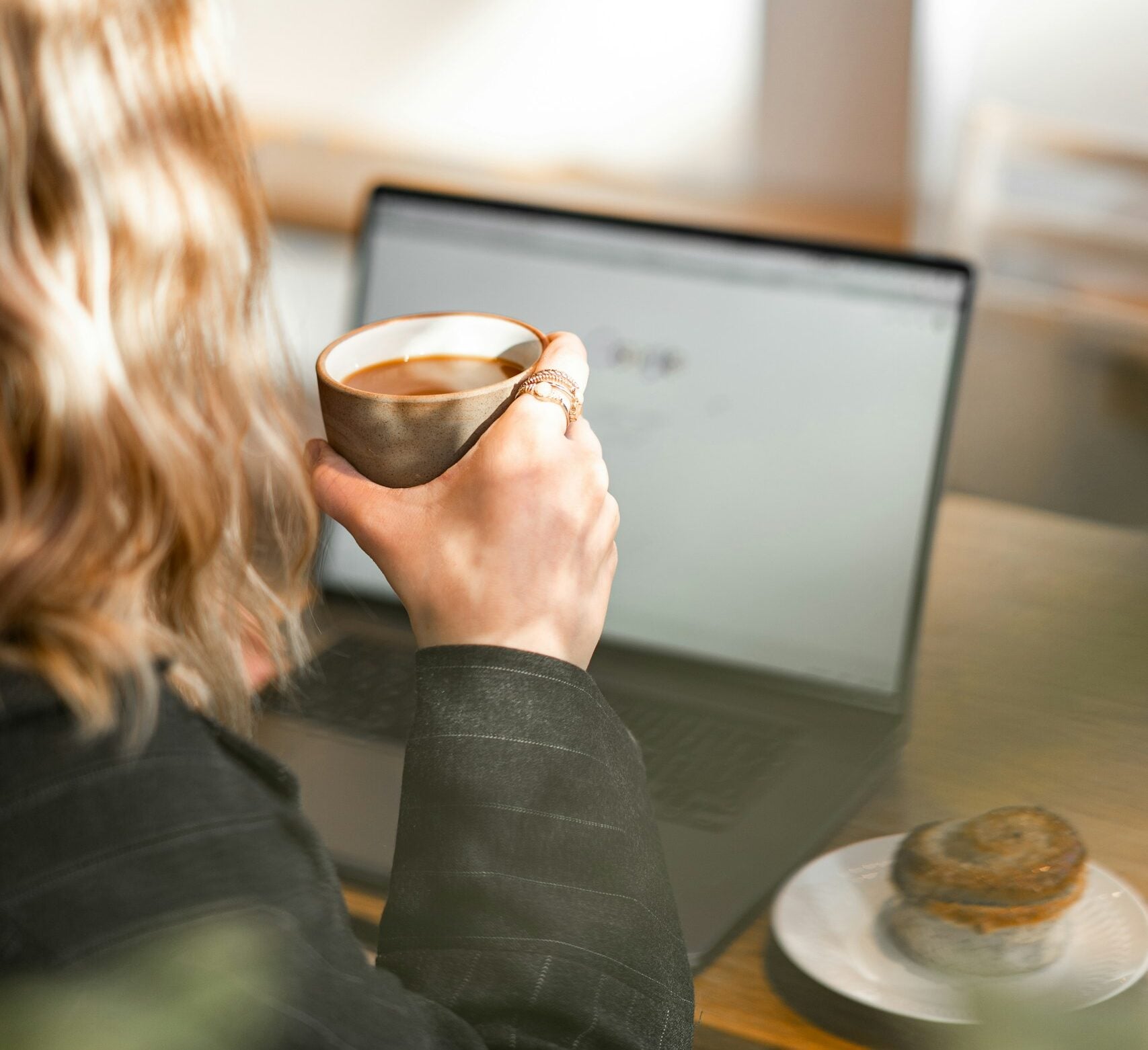 Blonde woman holding a cup of coffee waiting for her computer to load.