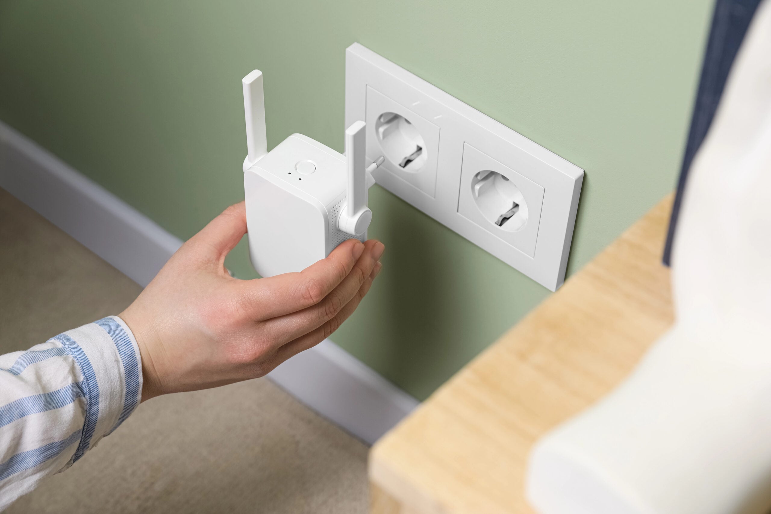 Woman inserting wireless Wi-Fi repeater into power socket indoors, closeup