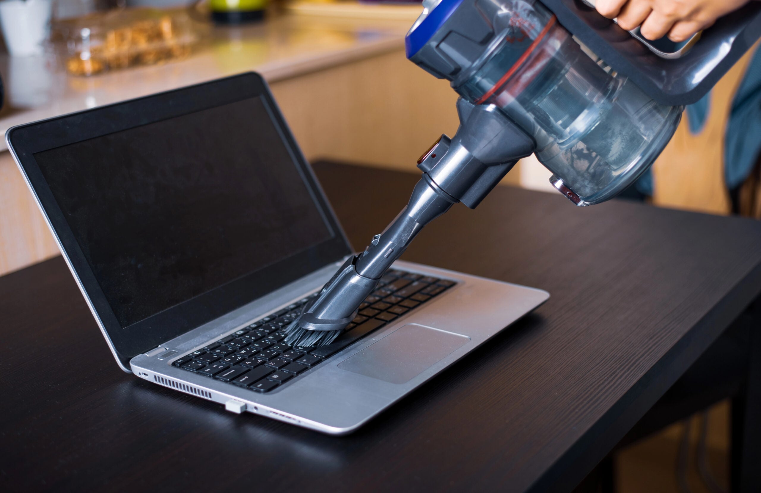 Woman vacuuming dust of a laptop with cordless vacuum cleaner