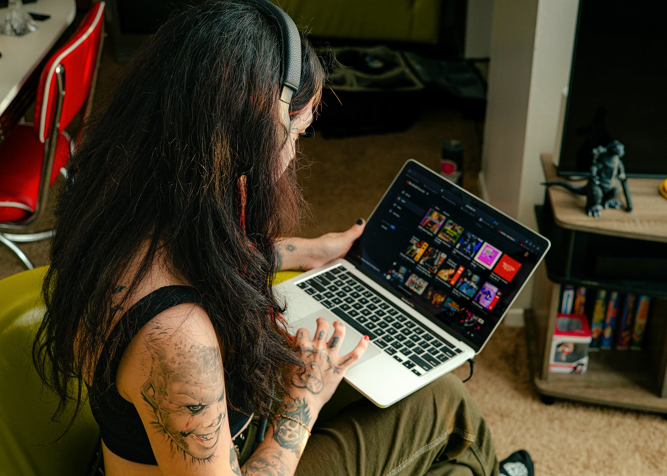 Woman with tattoos and headphones looking at music library on a laptop